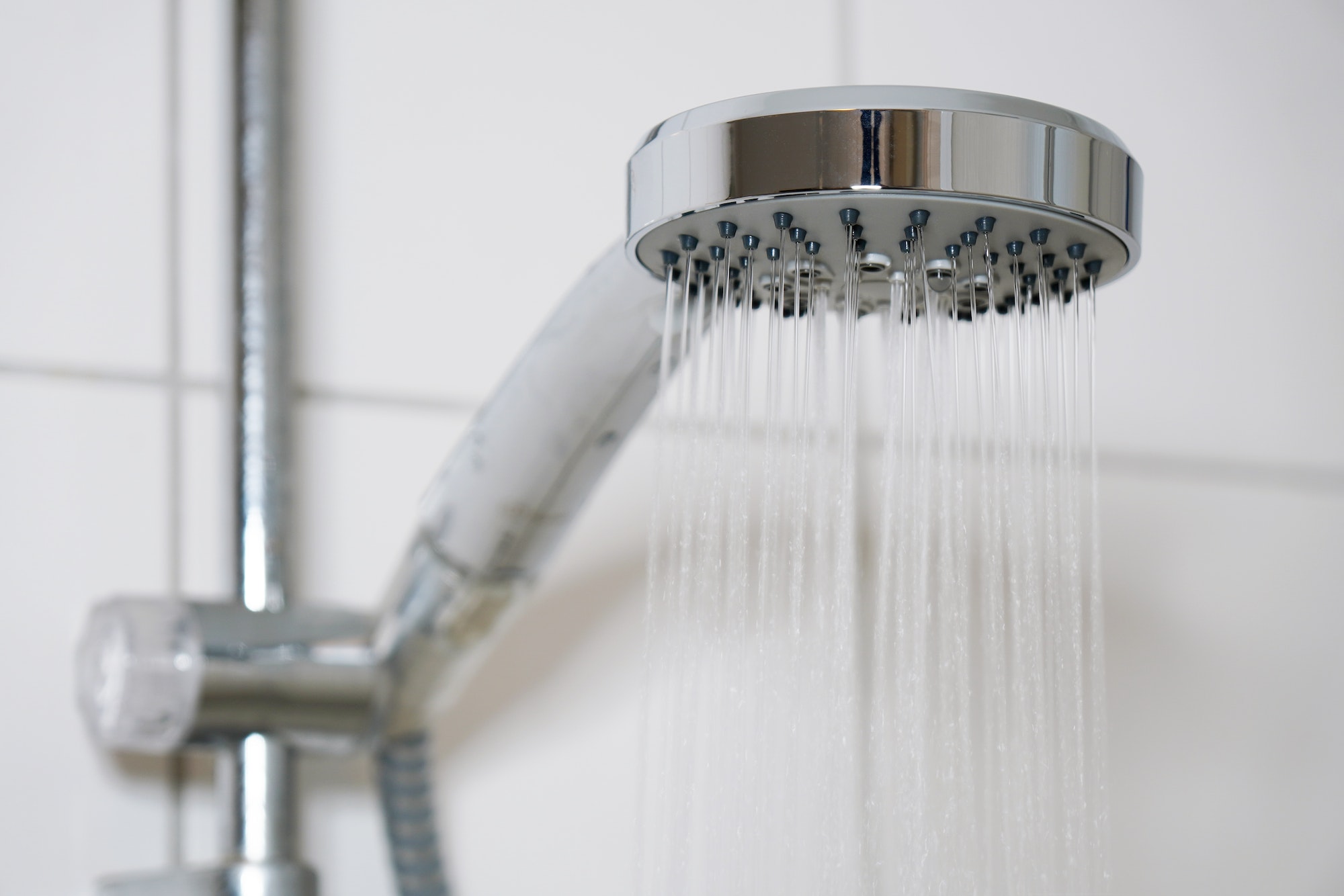 shower with modern showerhead and running water in domestic bathroom close-up